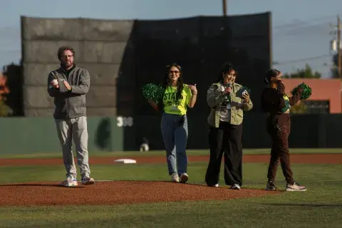 SMU College of Nursing Dean Steven Rush prepares to throw the ceremonial first pitch alongside event staff and hosts on the pitcher’s mound.