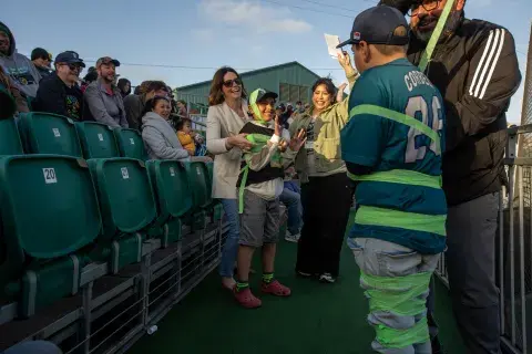 Attendees at the Oakland Ballers game laugh and cheer as children are playfully wrapped in green gauze during a health-themed game hosted by Samuel Merritt University.