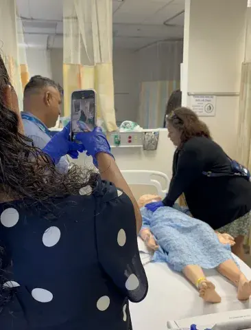 One prospective student takes a photo of two prospective students performing CPR on a "patient" in the simulation lab