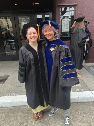 Two people dressed in graduation caps and gowns outdoors.
