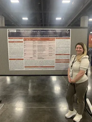 A student stands next to a large academic poster titled “Minimally Invasive Surgery in Trauma: A Systematic Review,” representing Samuel Merritt University’s College of Podiatric Medicine.