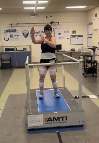 A student wearing motion sensors on her limbs and a headband stands on a treadmill in a biomechanics lab at Samuel Merritt University.