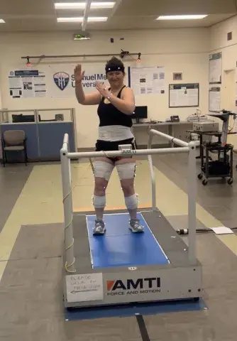 A student wearing motion sensors on her limbs and a headband stands on a treadmill in a biomechanics lab at Samuel Merritt University.