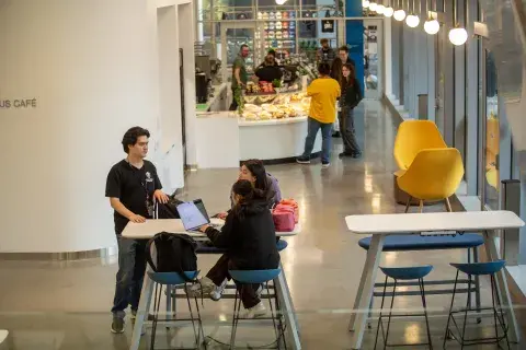Three students sitting at tables and talking near the campus cafe
