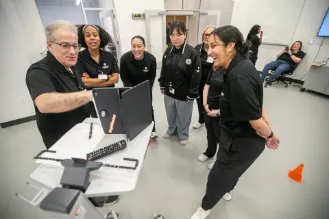 Student all gather around a doctor who is pointing to a screen.