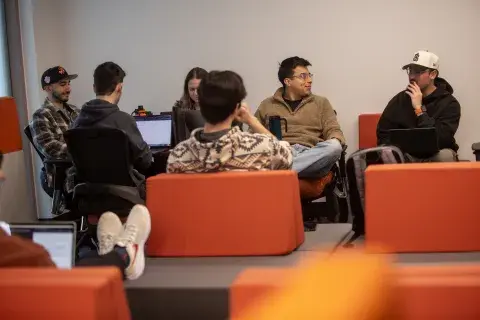 Students sitting together in lounge space with orange chairs