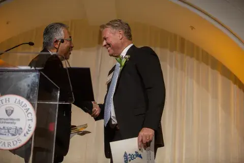 Two individuals shake hands on stage during an awards presentation at the Samuel Merritt University Health Impact Awards.
