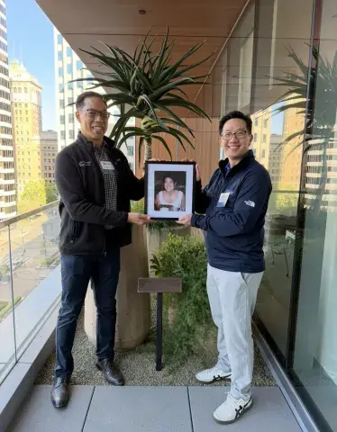 Two people in front of memorial garden holding photo of Tracey Teruya