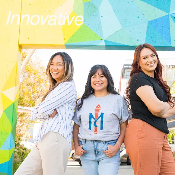Students pose in front of Oakland campus mural.
