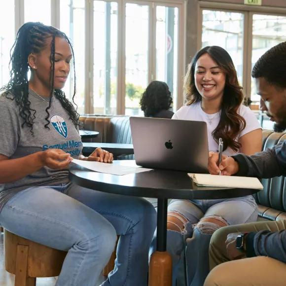 Three students in street clothes studying at a cafe