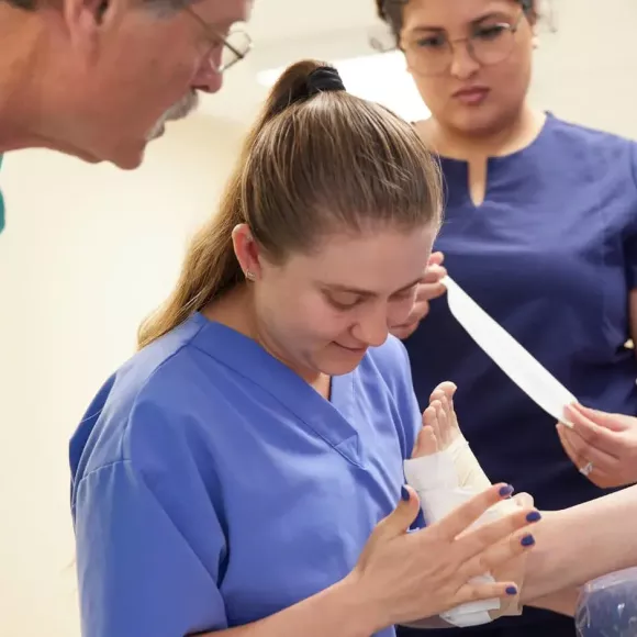 Student wrapping foot with Doctor observing