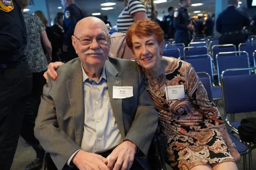 Two attendees smile for a photo while seated together at a community event.
