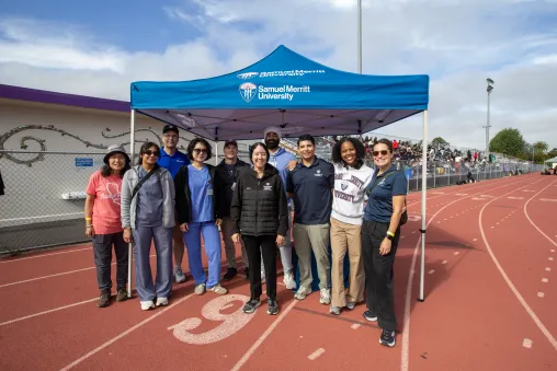 Students and faculty members of SMU stand on a track outdoors in front of blue SMU tent.