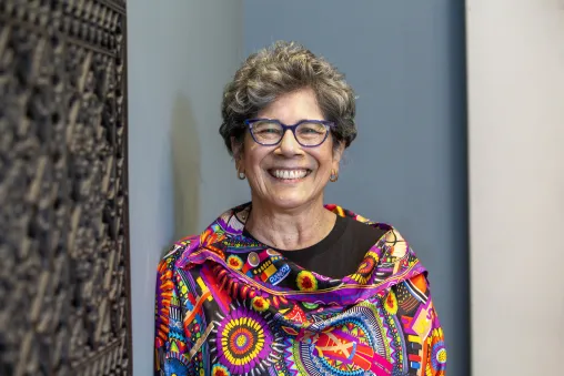 Board member wearing colorful top and glasses standing in front of a blue, white and brown background