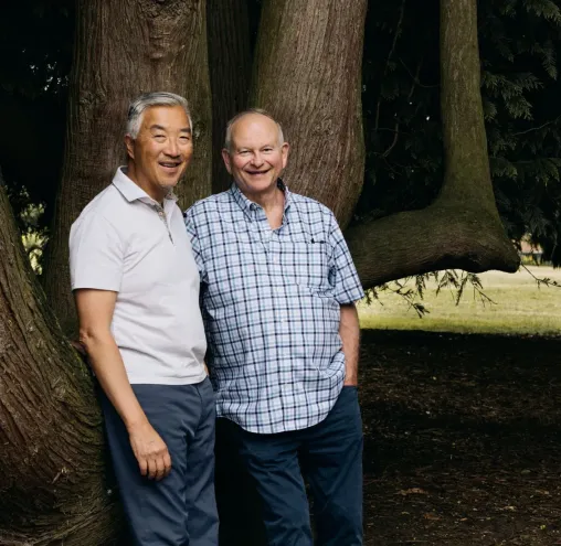 Two men standing by a tree smiling at the camera