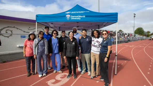 Students and faculty members of SMU stand on a track outdoors in front of blue SMU tent.