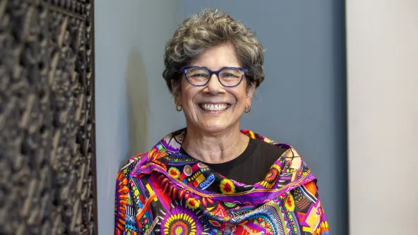 Board member wearing colorful top and glasses standing in front of a blue, white and brown background