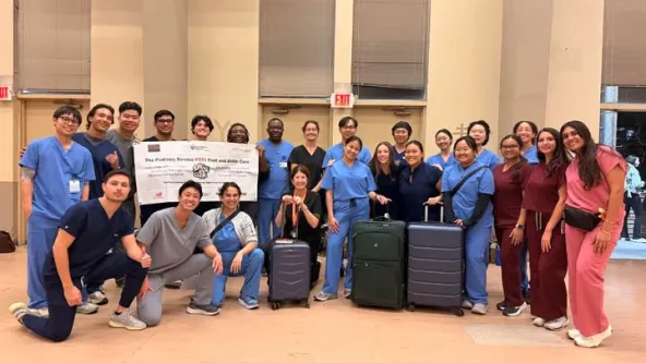 Group photo of students in scrubs with two suitcases in front of them and a banner behind
