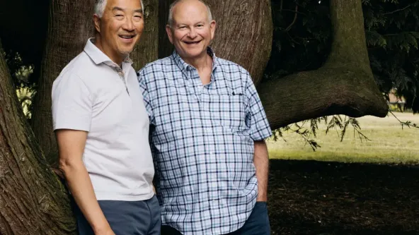 Two men standing by a tree smiling at the camera
