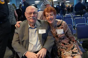 Two attendees smile for a photo while seated together at a community event.