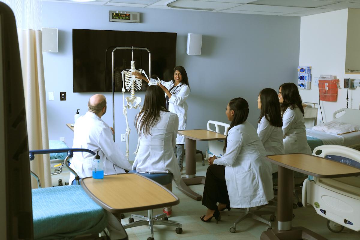Professor and students in training room looking at a skeleton