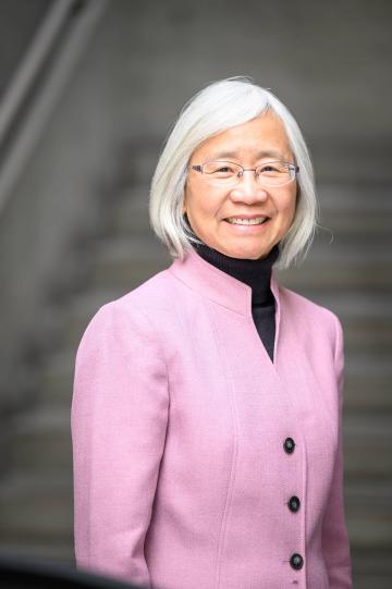 Dean Evaon Wong Kim wearing a pink blazer and black turtle neck. She has short white hair and glasses.