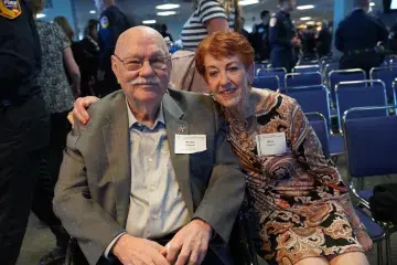 Two attendees smile for a photo while seated together at a community event.
