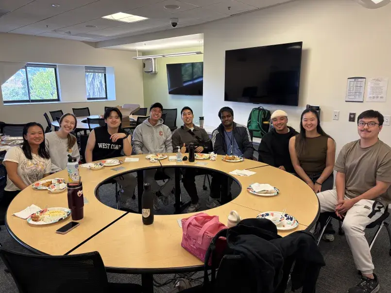Ten student tutors sit around table with plates of food, smiling for a photo.