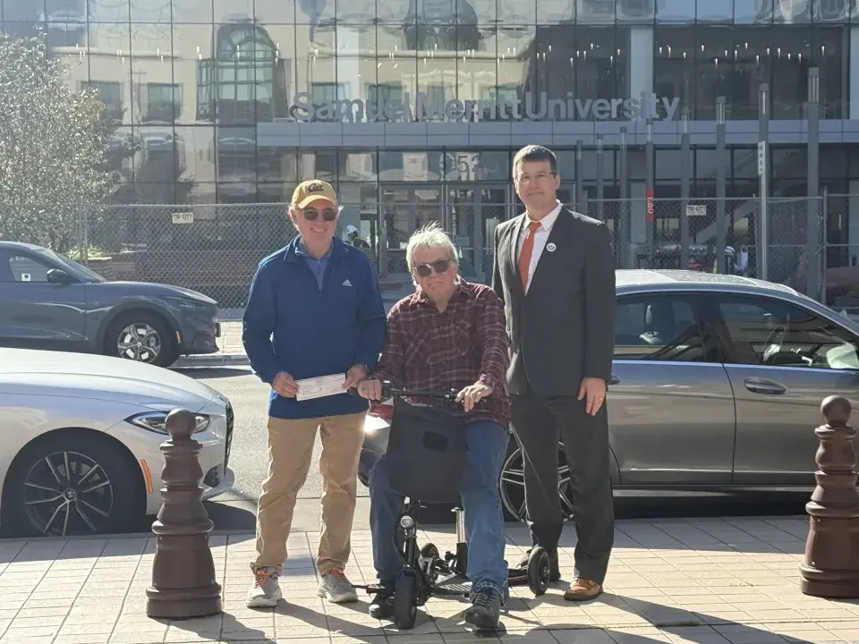 Three individual outside the SMU Oakland campus. One is seated on a mobility scooter.