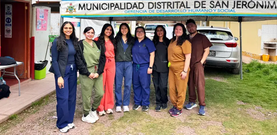 Group of students wearing scrubs posing for photo outside with Spanish sign in background
